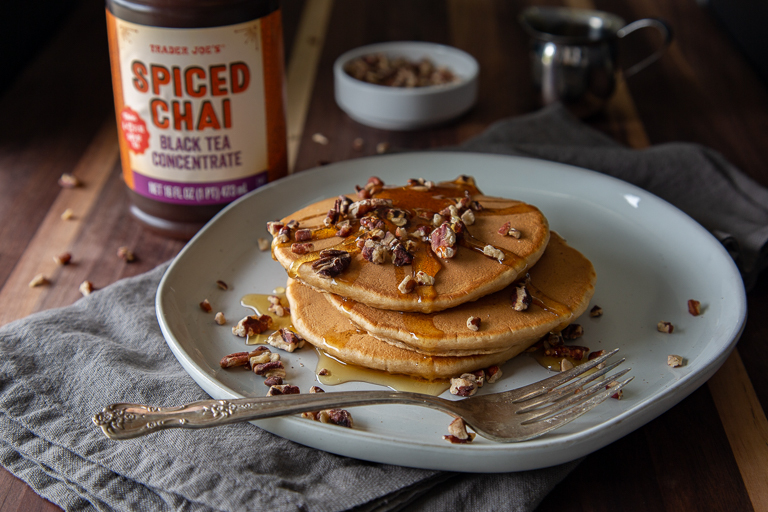 plate of pancakes with syrup and nuts on top with Trader Joe's Spiced Chai Concentrate bottle in the background
